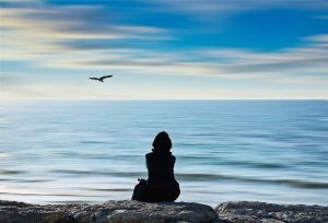 mulher sentaada na pedra e olhando para o mar após aprender como controlar a ansiedade